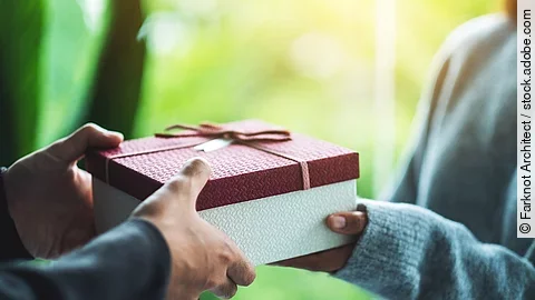 Nahaufnahme von einer Person die an eine andere Person ein Geschenk übergibt.
