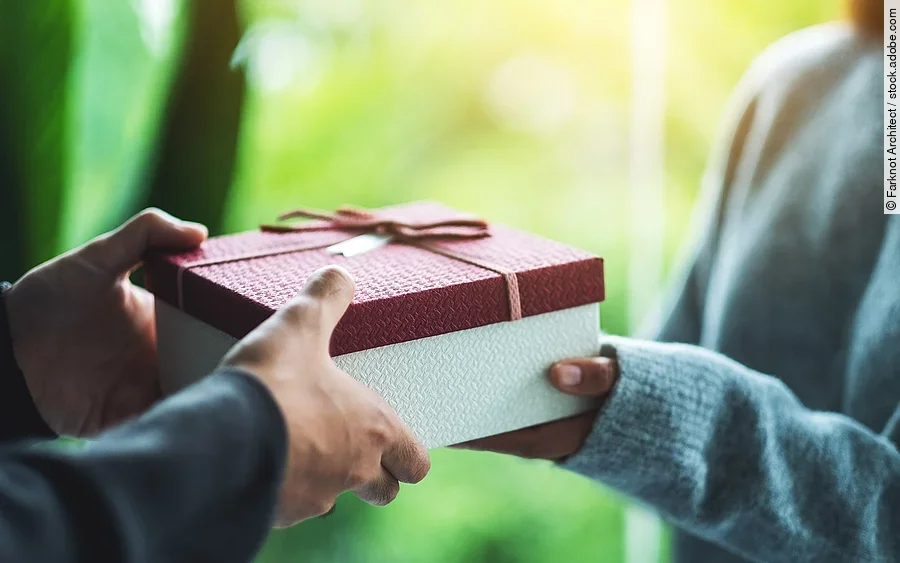 Nahaufnahme von einer Person die an eine andere Person ein Geschenk übergibt.