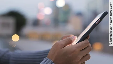 Im Fokus ist ein Smartphone, welches von zwei Händen einer Person festgehalten wird.