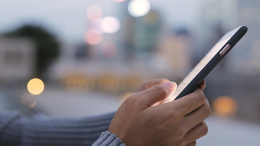 Im Fokus ist ein Smartphone, welches von zwei Händen einer Person festgehalten wird.