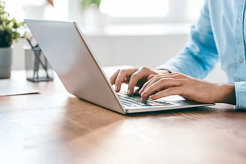 Eine Person sitzt vor einem Laptop und hat die Hände auf der Tastatur. 