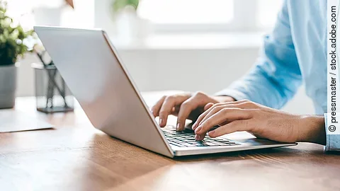 Eine Person sitzt vor einem Laptop und hat die Hände auf der Tastatur. 