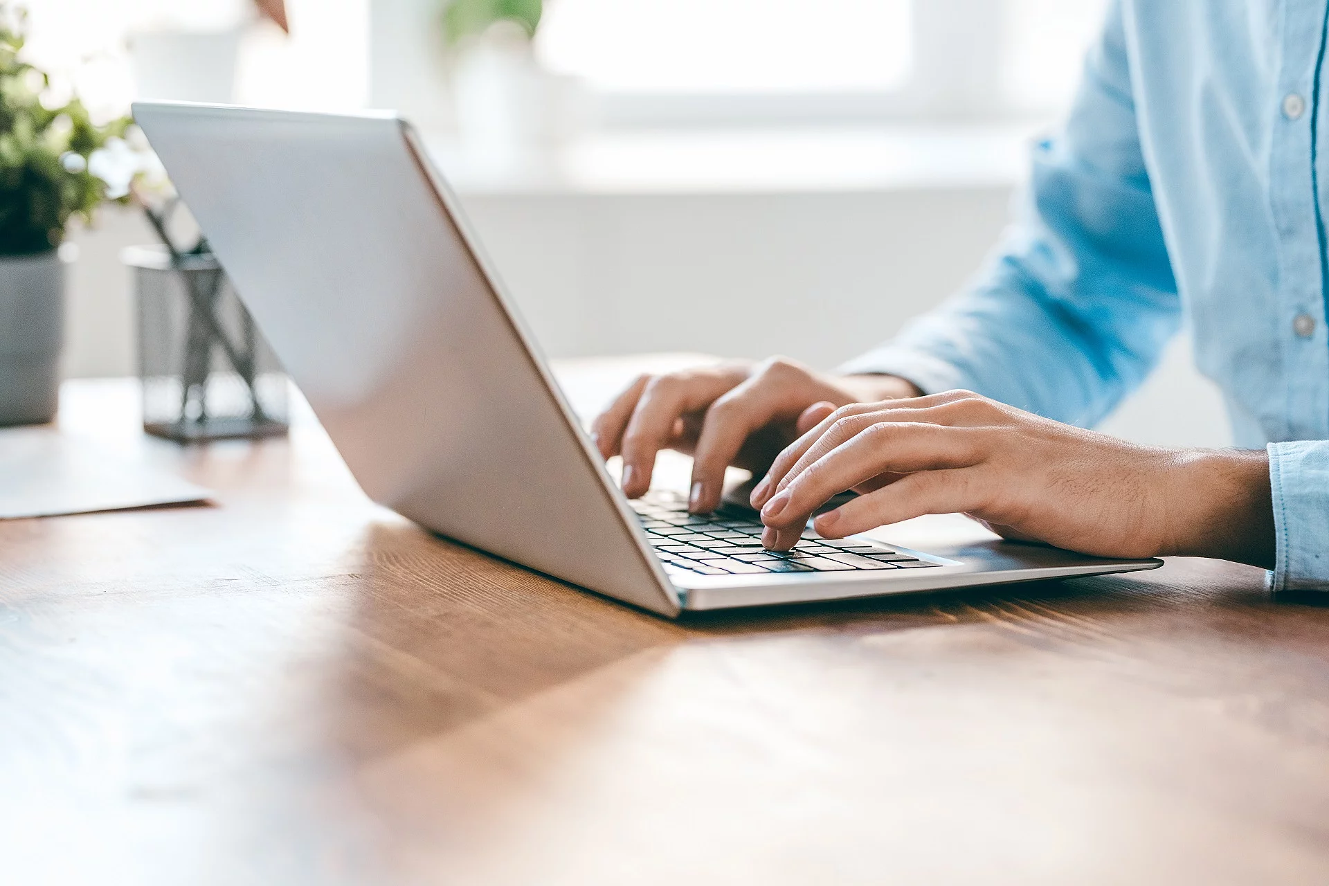 Eine Person sitzt vor einem Laptop und hat die Hände auf der Tastatur. 