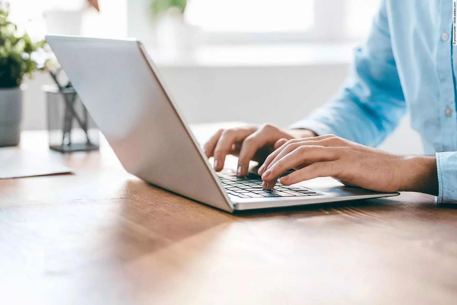 Eine Person sitzt vor einem Laptop und hat die Hände auf der Tastatur. 