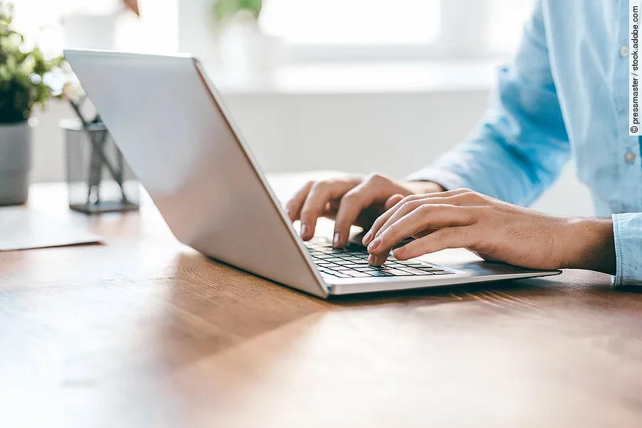 Eine Person sitzt vor einem Laptop und hat die Hände auf der Tastatur. 