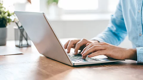 Eine Person sitzt vor einem Laptop und hat die Hände auf der Tastatur. 