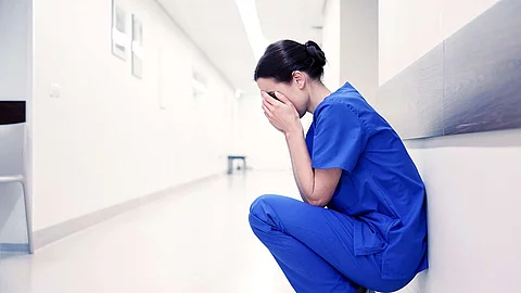 sad or crying female nurse at hospital corridor