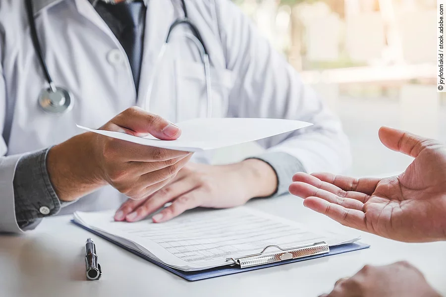 Eine Person mit weißen Kittel übergibt ein Dokument an eine andere Person.