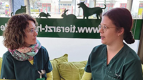 Dorothee Köstler sitzt mit einer Teamkollegin auf einer Bank und redet mit ihr.