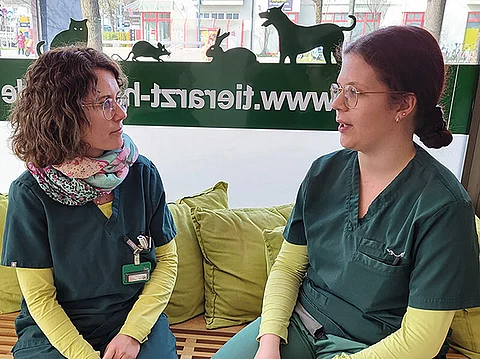 Dorothee Köstler sitzt mit einer Teamkollegin auf einer Bank und redet mit ihr.