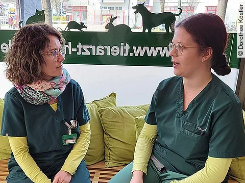 Dorothee Köstler sitzt mit einer Teamkollegin auf einer Bank und redet mit ihr.