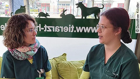 Dorothee Köstler sitzt mit einer Teamkollegin auf einer Bank und redet mit ihr.