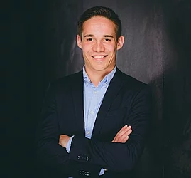 Philipp Rolzhäuser steht lächelnd mit verschränkten Armen vor einem dunklen Hintergrund.