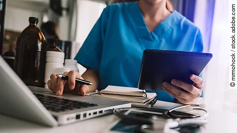 Eine Person sitzt an einem Schreibtisch mit Laptop und Tablet.