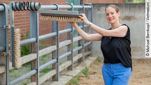 Borbala Foris steht lächelnd in einem Auslauf für Rinder und hält eine Bürste zum Kratzen für die Tiere fest. Dabei sieht sie glücklich aus. Borbala Foris steht lächelnd in einem Auslauf für Rinder und hält eine Bürste zum Kratzen für die Tiere fest. Dabei sieht sie glücklich aus.