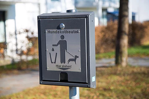 Eine Kotbeutelspender hängt in Wohnanlage und weist darauf hin, dass man die Hinterlassenschaften seines Hundes entfernt soll.