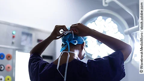 Eine Person steht im OP und bindest sich die OP-Maske zu.