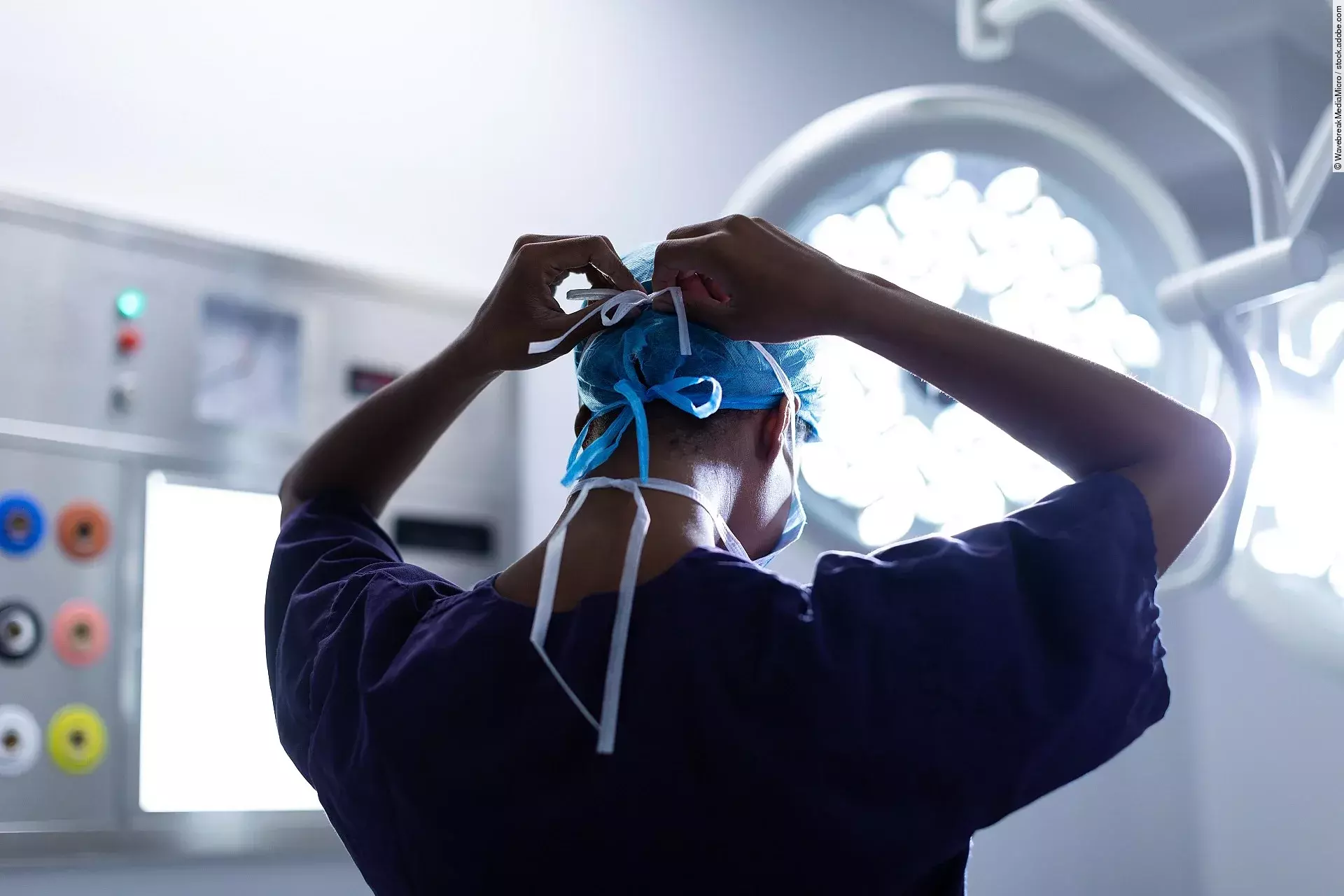 Female surgeon wearing surgical mask in operation theater at hos Eine Person steht im OP und bindest sich die OP-Maske zu.