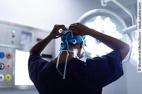 Eine Person steht im OP und bindest sich die OP-Maske zu.