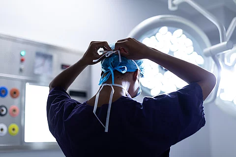 Female surgeon wearing surgical mask in operation theater at hos Eine Person steht im OP und bindest sich die OP-Maske zu.