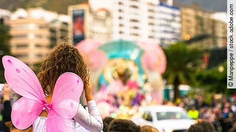 Verkleidete Personen schauen einem Karnevalsumzug zu.