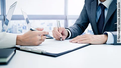 Zwei Personen sitzen sich gegenüber an einem Tisch. Zwischen ihnen liegen Dokumente..