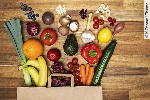 Eine Einkaufstasche voller gesundem Obst und Gemüse liegt ordentlich ausgebreitet auf dem Tisch.
