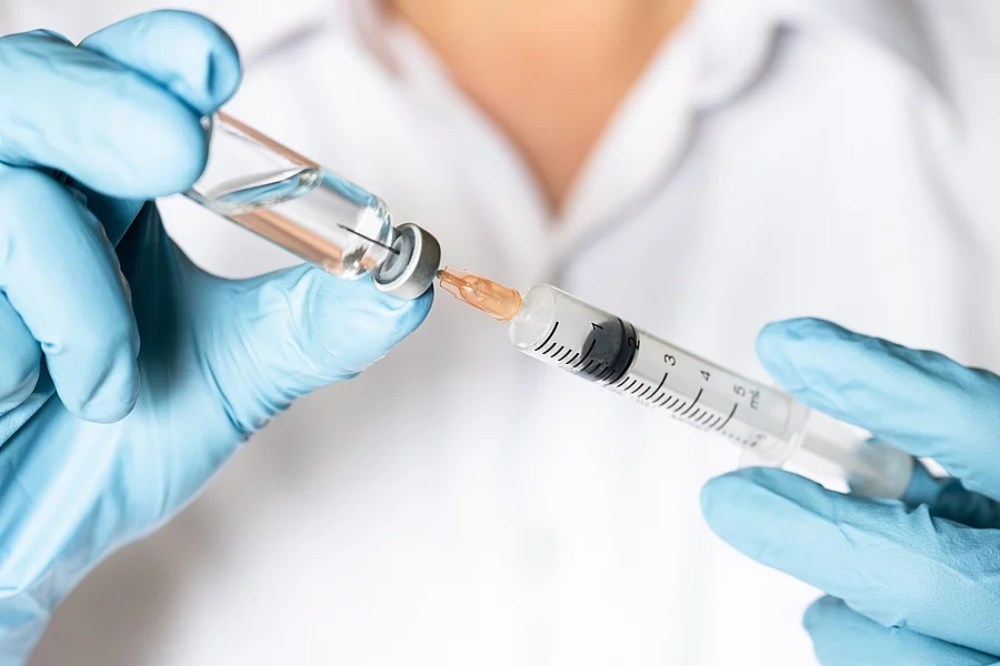 Nurse or doctor hand in blue glove holding flu, measles vaccine Ein*e Ärzt*in zieht eine Impfung auf.