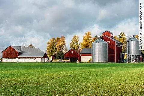 Ein Bauernhof in klassichem Schwedenrot hat eine große grünen Wiese und neu aussehende Silos.