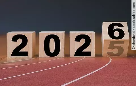 Auf Holzblöcken steht die Jahreszahl 2025, die letzte Zahl kippt auf die Zahl 6. Die Holzklötze sind braun und die Schrift ist in schwarz. Die Blöcke sind auf einer Laufbahn projiziert.