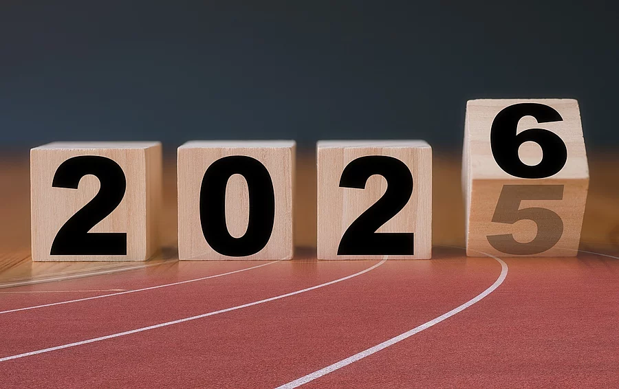 Auf Holzblöcken steht die Jahreszahl 2025, die letzte Zahl kippt auf die Zahl 6. Die Holzklötze sind braun und die Schrift ist in schwarz. Die Blöcke sind auf einer Laufbahn projiziert.