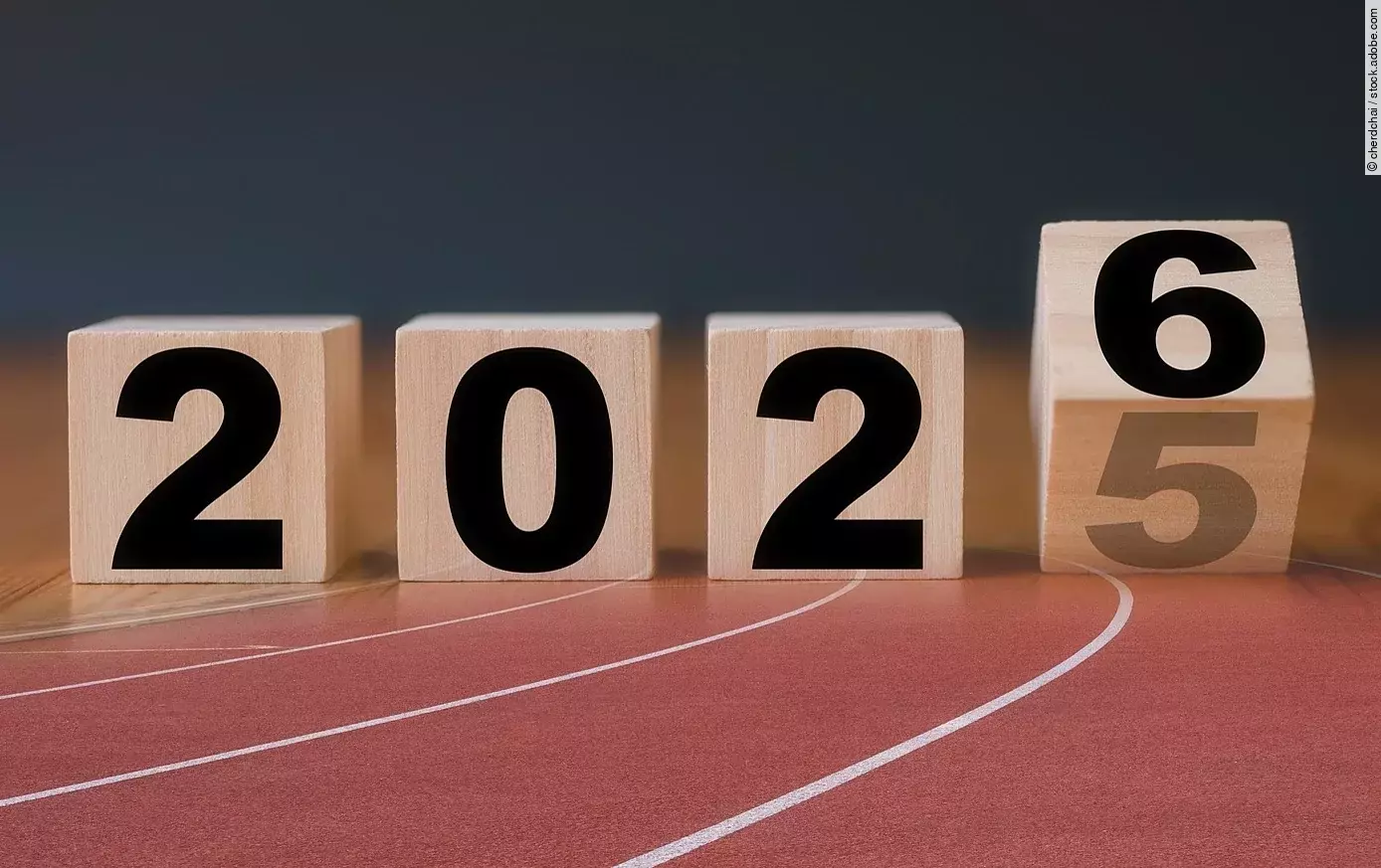 Auf Holzblöcken steht die Jahreszahl 2025, die letzte Zahl kippt auf die Zahl 6. Die Holzklötze sind braun und die Schrift ist in schwarz. Die Blöcke sind auf einer Laufbahn projiziert.