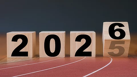 Auf Holzblöcken steht die Jahreszahl 2025, die letzte Zahl kippt auf die Zahl 6. Die Holzklötze sind braun und die Schrift ist in schwarz. Die Blöcke sind auf einer Laufbahn projiziert.