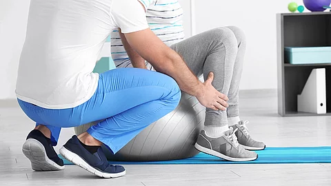 Ein Physiotherapeut arbeitet mit einer Person an einem Gymnastikball. 