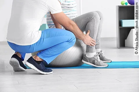 Ein Physiotherapeut arbeitet mit einer Person an einem Gymnastikball. 