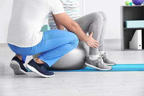 Ein Physiotherapeut arbeitet mit einer Person an einem Gymnastikball. 