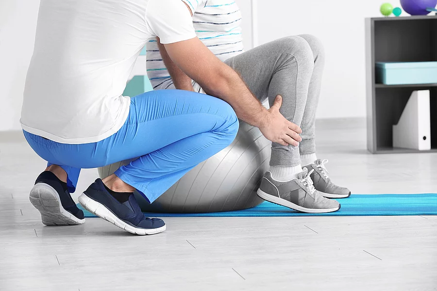 Ein Physiotherapeut arbeitet mit einer Person an einem Gymnastikball.