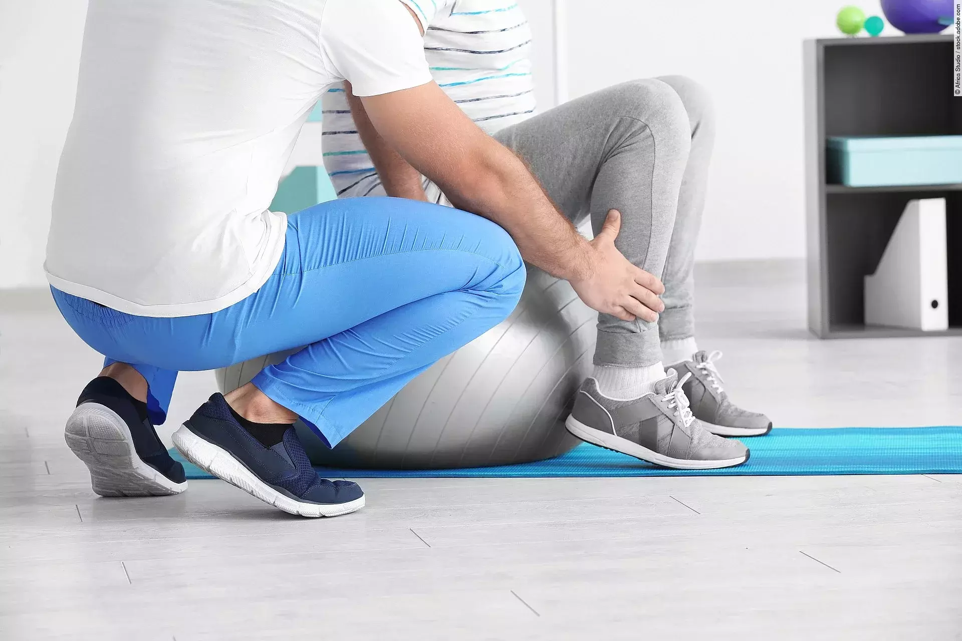 Ein Physiotherapeut arbeitet mit einer Person an einem Gymnastikball. 