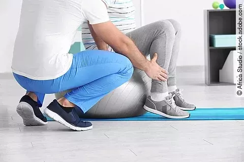 Ein Physiotherapeut arbeitet mit einer Person an einem Gymnastikball. 