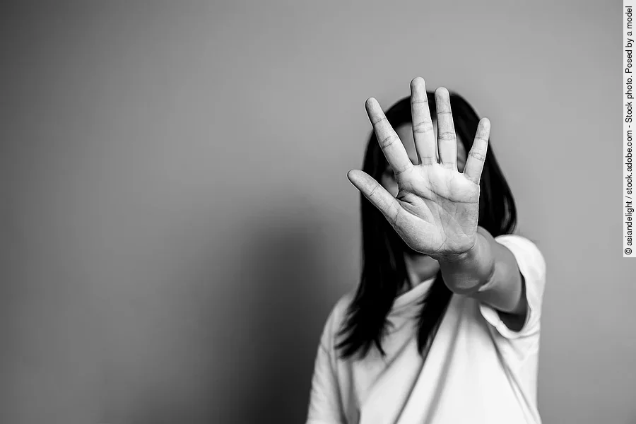 Auf einer schwarz-weiß Fotografie streckt eine Frau schützend den Arm aus und signalisiert mit ihrer Hand ein Stop-Signal. Auf einer schwarz-weiß Fotografie streckt eine Frau schützend den Arm aus und signalisiert mit ihrer Hand ein Stop-Signal.