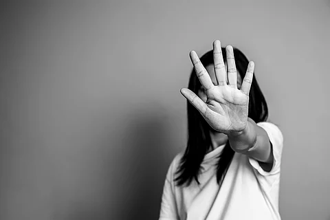 Auf einer schwarz-weiß Fotografie streckt eine Frau schützend den Arm aus und signalisiert mit ihrer Hand ein Stop-Signal. 