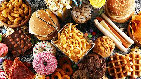 Ein Tisch ist voll mit verschiedenem Fastfood - vom Donuts über Pommes bis hin zu Burgern und Hot Dogs.