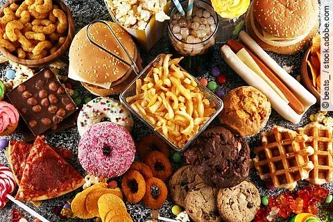 Ein Tisch ist voll mit verschiedenem Fastfood - vom Donuts über Pommes bis hin zu Burgern und Hot Dogs.