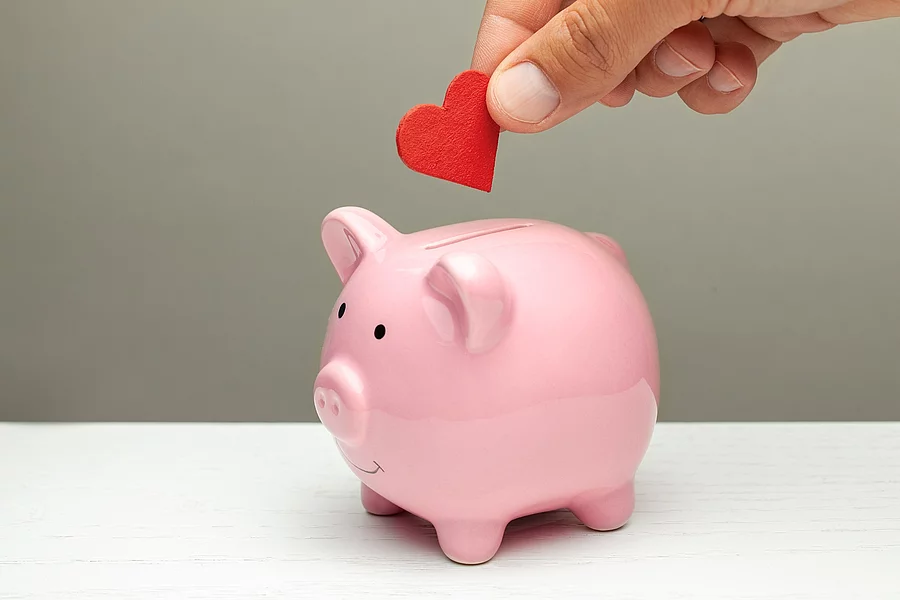 Spenden aus Liebe und Mitgefühl. Ein Mensch steckt ein Herz aus Filz in ein Sparschwein.