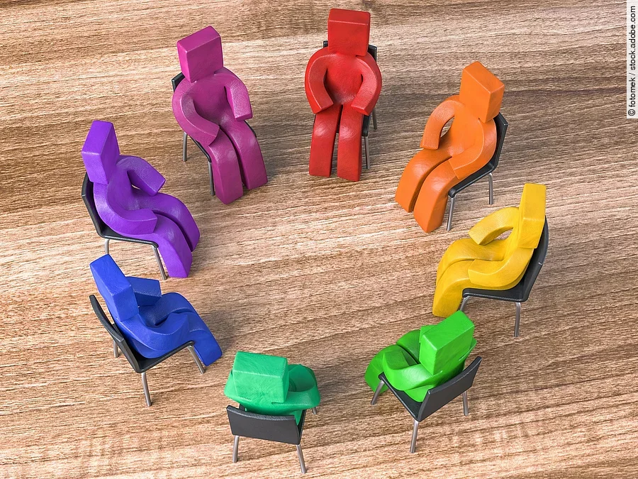 Bunte Knetfiguren in Rot-, Blau- und Grüntönen sitzen in einem Stuhlkreis auf schwarzen Stühlen. Bunte Knetfiguren in Rot-, Blau- und Grüntönen sitzen in einem Stuhlkreis auf schwarzen Stühlen.