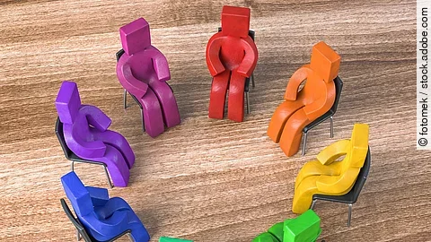 Bunte Knetfiguren in Rot-, Blau- und Grüntönen sitzen in einem Stuhlkreis auf schwarzen Stühlen. Bunte Knetfiguren in Rot-, Blau- und Grüntönen sitzen in einem Stuhlkreis auf schwarzen Stühlen.