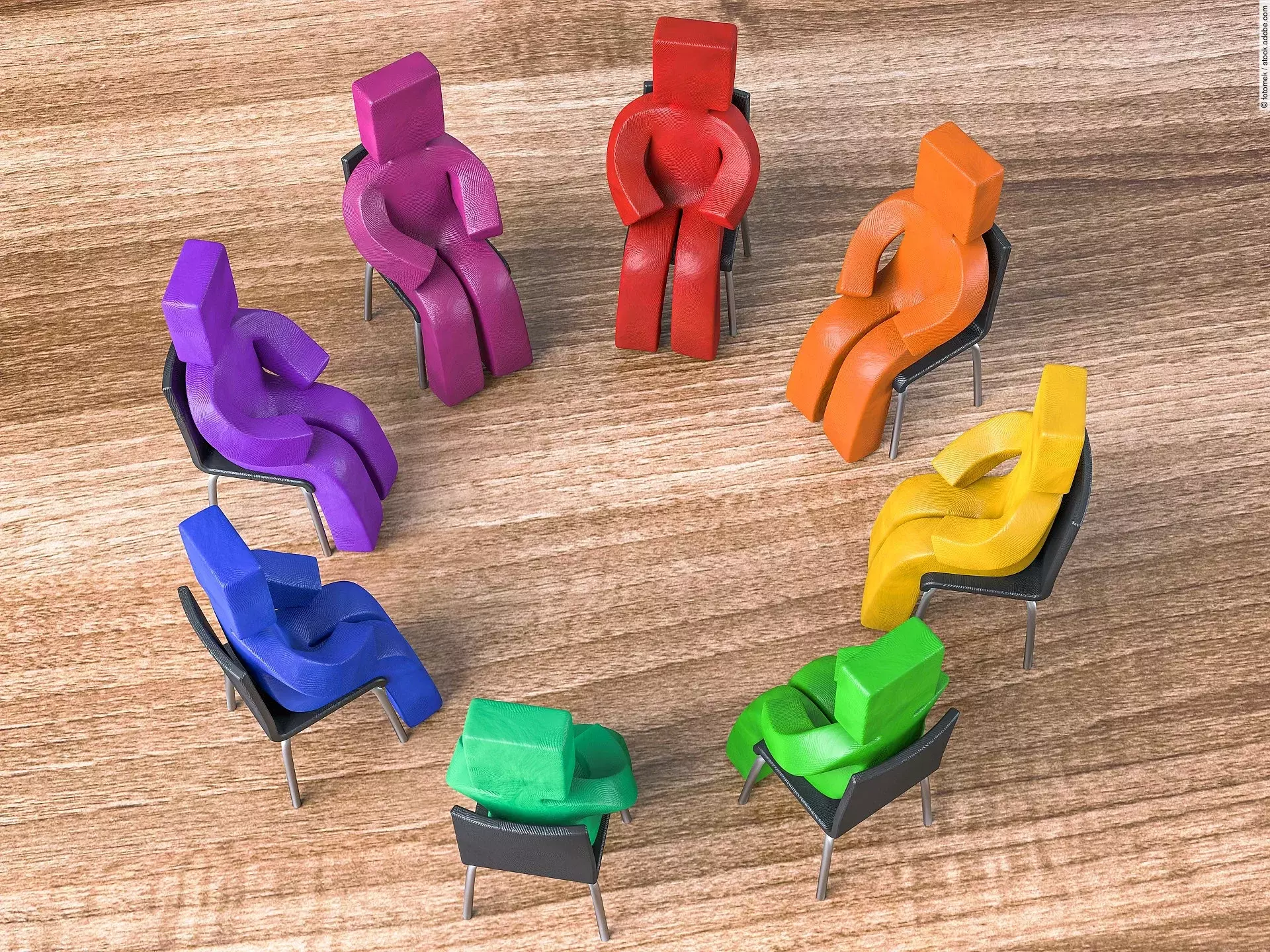 Bunte Knetfiguren in Rot-, Blau- und Grüntönen sitzen in einem Stuhlkreis auf schwarzen Stühlen.