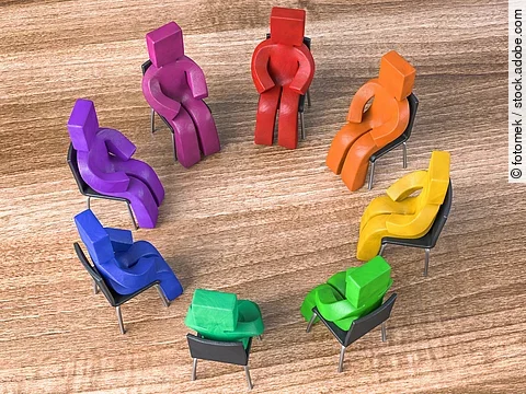 Bunte Knetfiguren in Rot-, Blau- und Grüntönen sitzen in einem Stuhlkreis auf schwarzen Stühlen.