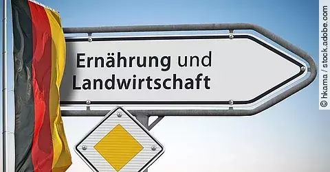 Ein weißes Straßenschild weist den Weg zum Bundesministerium für Ernährung und Landwirtschaft. Daneben hängt eine Deutschlandflagge.