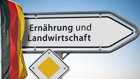 Ein weißes Straßenschild weist den Weg zum Bundesministerium für Ernährung und Landwirtschaft. Daneben hängt eine Deutschlandflagge.